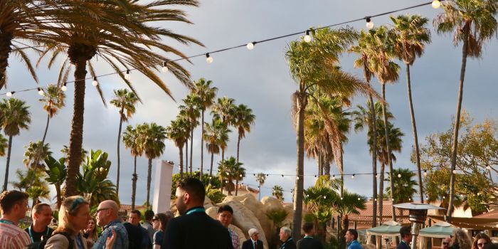 Reflecting on ascend 2024: resolver security summit 3 "attendees networking under palm trees at ascend 2024, with string lights creating a festive atmosphere at mission bay resort. "