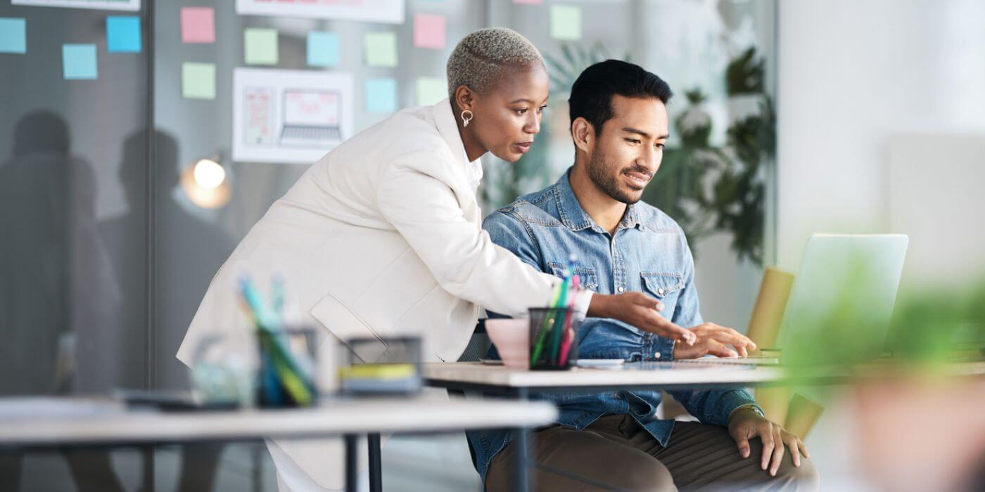 Two professionals in an office environment collaborating on a computer, discussing details related to whistleblower software.