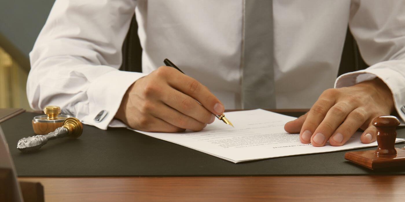 A close-up of a professional signing a legal document at a desk, symbolizing workplace violence laws and their enforcement, with a wax seal and pen in the foreground for emphasis.