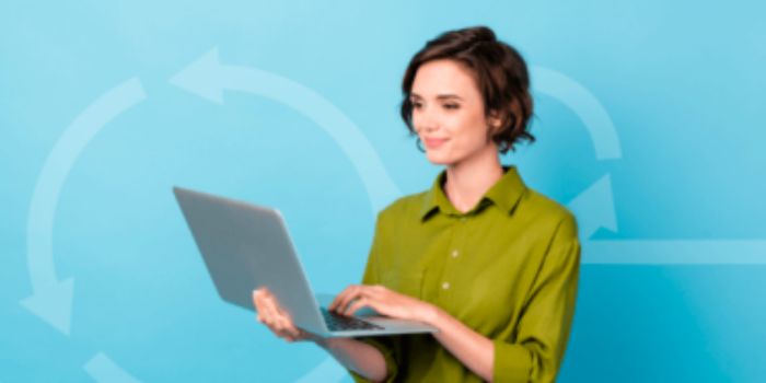 Agile grc woman in green shirt holding a laptop in front of a pale blue background
