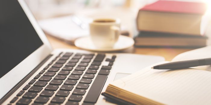 Laptop, open notebook with pen, coffee cup, and stacked books on a desk—visual metaphor for comparing enterprise risk management vs. Traditional risk management approaches.