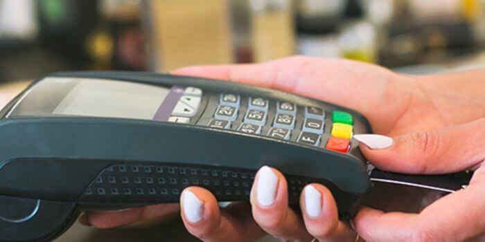 Woman with white manicured nails inserting credit card in card reading machine representing retail inventory shrink