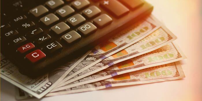 A calculator and four $100 bills representing risks for financial institutions