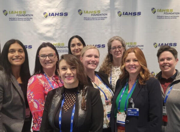 Group photo of resolver attendees smiling at the iahss 2024 conference in front of a promotional banner.