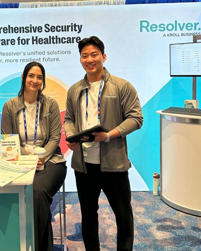 Two people, a woman and a man, are posing at a booth for resolver's healthcare security software at the iahss 2024 conference. The backdrop highlights the software's key features, and the display includes a section labeled "common challenges faced in hospitals," focusing on issues like vulnerable patients, security regulations, and workplace violence.
