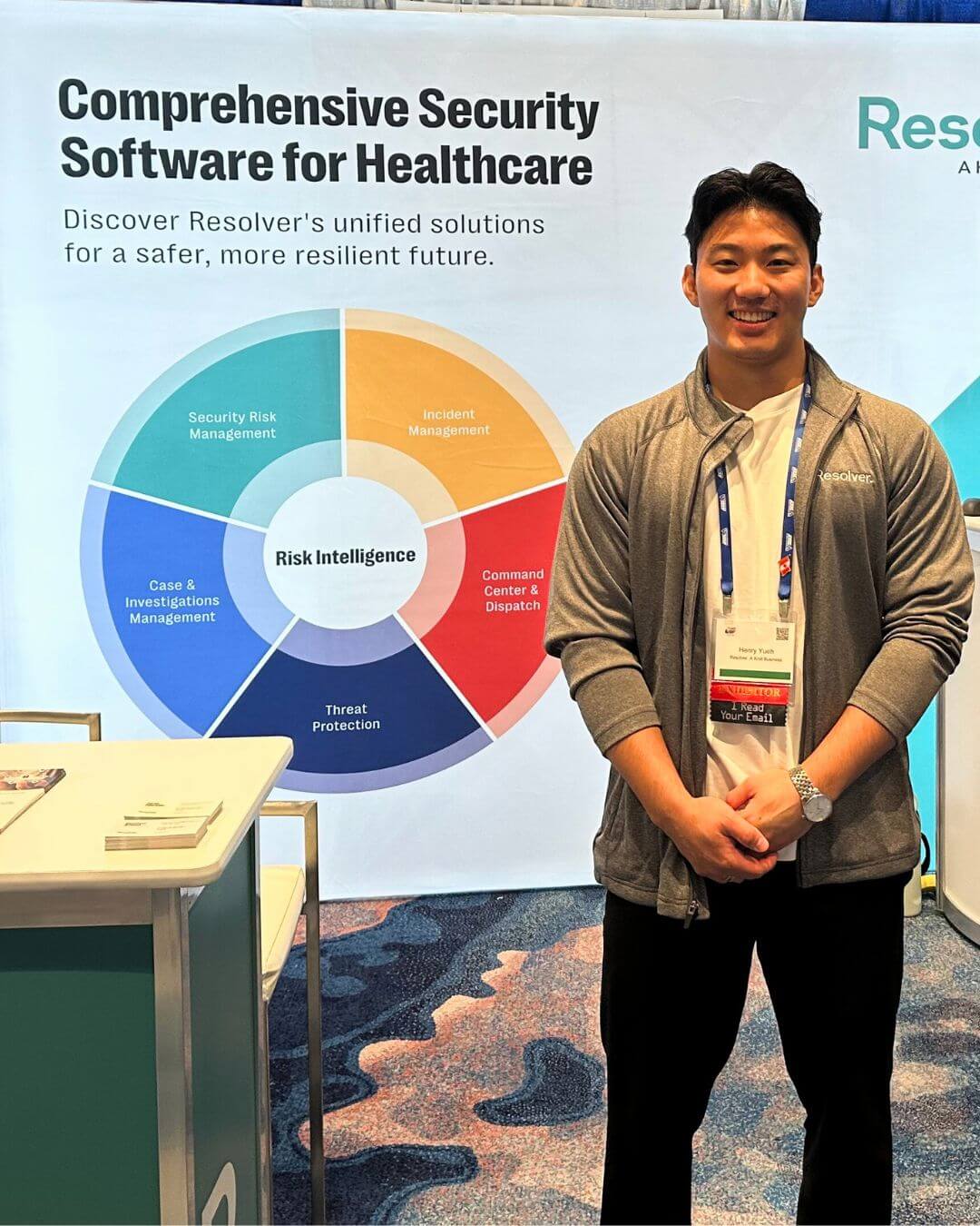 A resolver representative stands next to a booth at the iahss 2024 conference. Behind them is a display featuring a colorful wheel labeled "risk intelligence," highlighting various aspects of comprehensive security software for healthcare, including incident management, security risk management, and more.
