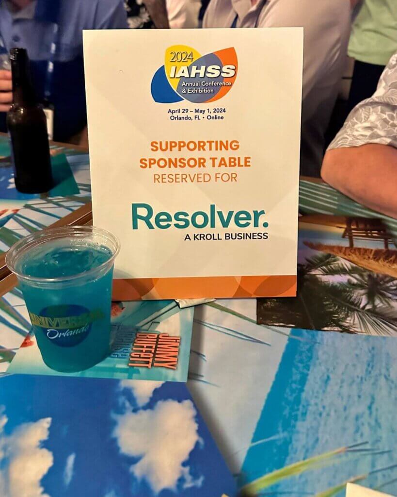 A close-up shot of a supporting sponsor table reserved for resolver at the iahss 2024 conference in orlando, florida. The table includes a colorful sign with the iahss logo and a blue drink with a universal studios orlando logo on the cup, creating a fun and branded atmosphere.