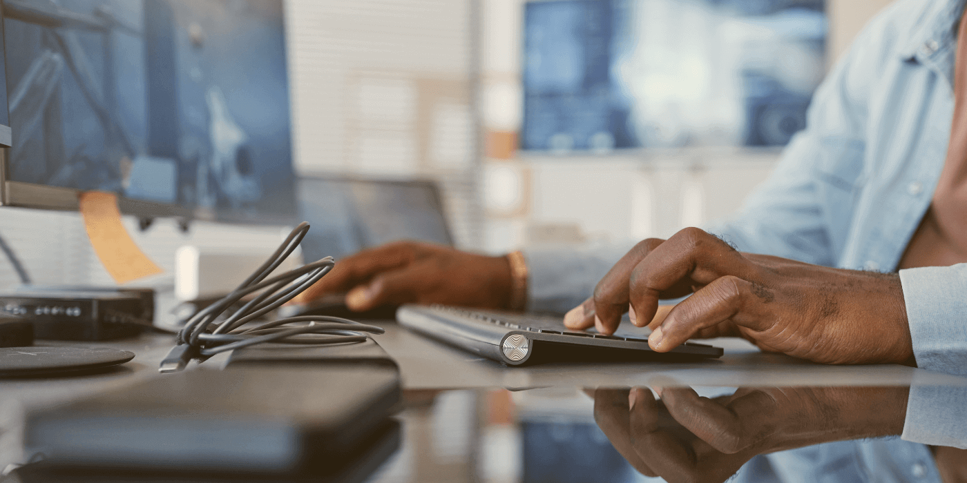 Close-up of a person typing on a keyboard at a desk with multiple computer monitors, representing a search for information on incident management software faq