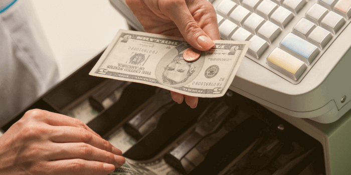 Male hands holding a five dollar us bill and a penny in one hand over a cash register, while removing a fifty dollar us bill representing retail employee theft