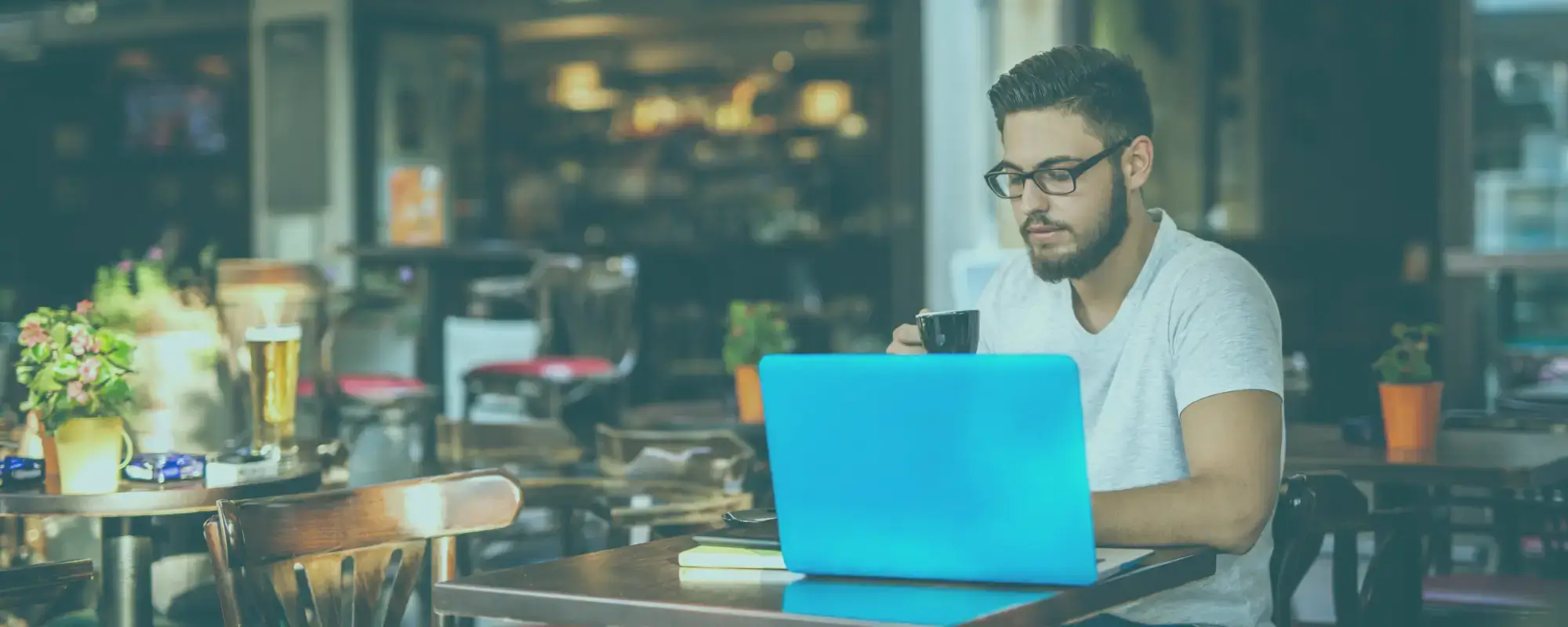 Man working on a blue laptop and mobile phone in a cafe representing the need for a remote work security policy